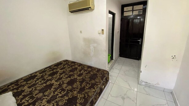 Ein Zimmer mit einem Bett, einer Klimaanlage, einer Tür und einem Fliesenboden.