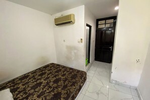 Una habitación con cama, aire acondicionado, una puerta y piso de baldosas.