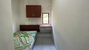 Ein kleiner, schmaler Raum mit einem Bett, einem Holzschrank und einem Fenster.