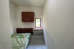 A small, narrow room with a bed, a wooden cabinet, and a window.