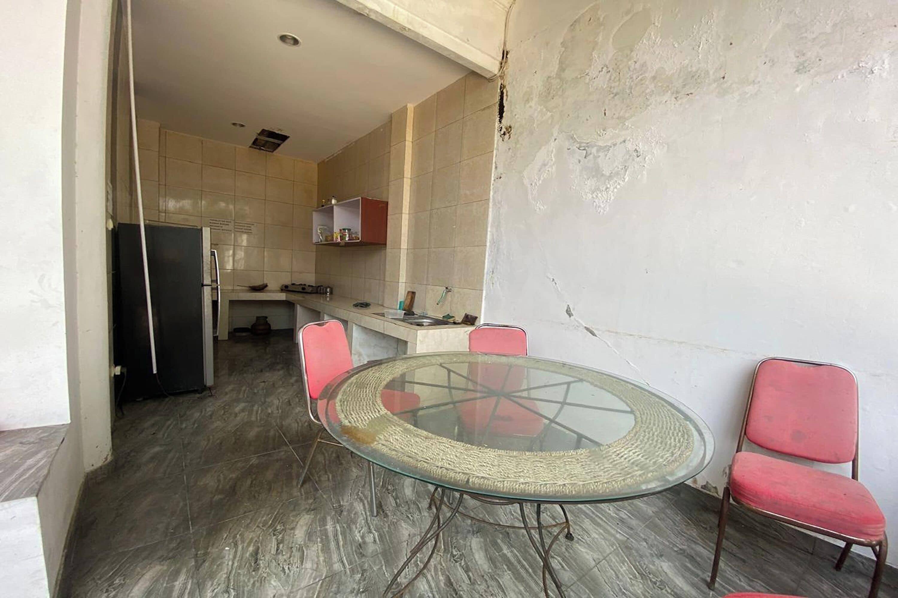 Cocina compacta con refrigerador, lavamanos y una pequeña encimera. Se ve una mesa de comedor con sillas y una butaca roja.