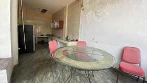 Eine kompakte Küche mit Kühlschrank, Spüle und einer kleinen Arbeitsplatte. Ein Esstisch mit Stühlen und ein roter Sessel sind zu sehen.