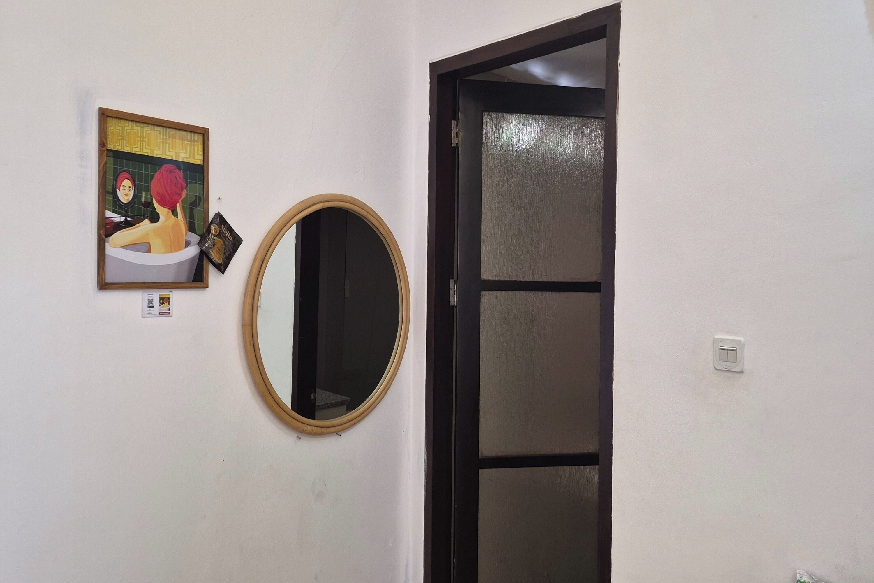 Una habitación con una puerta, un espejo fijado a la pared y un cuadro enmarco.