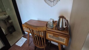 Une petite table en bois, avec une bouilloire et un pichet en verre, une chaise et une décoration murale.