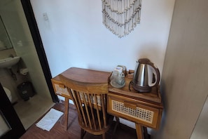 A small wooden table with a kettle and a glass pitcher, a chair, and a decorative wall hanging.