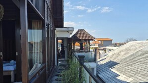 Ein Balkon mit Blick auf den Himmel, ein kleiner überdachter Bereich und ein Gebäude mit einem Ziegeldach.