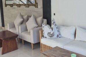 Una sala de estar moderna con un sofá gris, una mesa de centro de madera y una mesita auxiliar de mimbre.