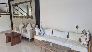 Un salon comprenant un canapé, des fauteuils, une table basse, un miroir et un escalier.