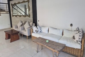 A living room with a sofa, armchairs, a coffee table, a mirror, and a staircase.