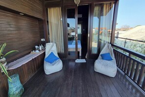 Un balcón con dos sillones tipo puffs, piso de madera y vistas del entorno.