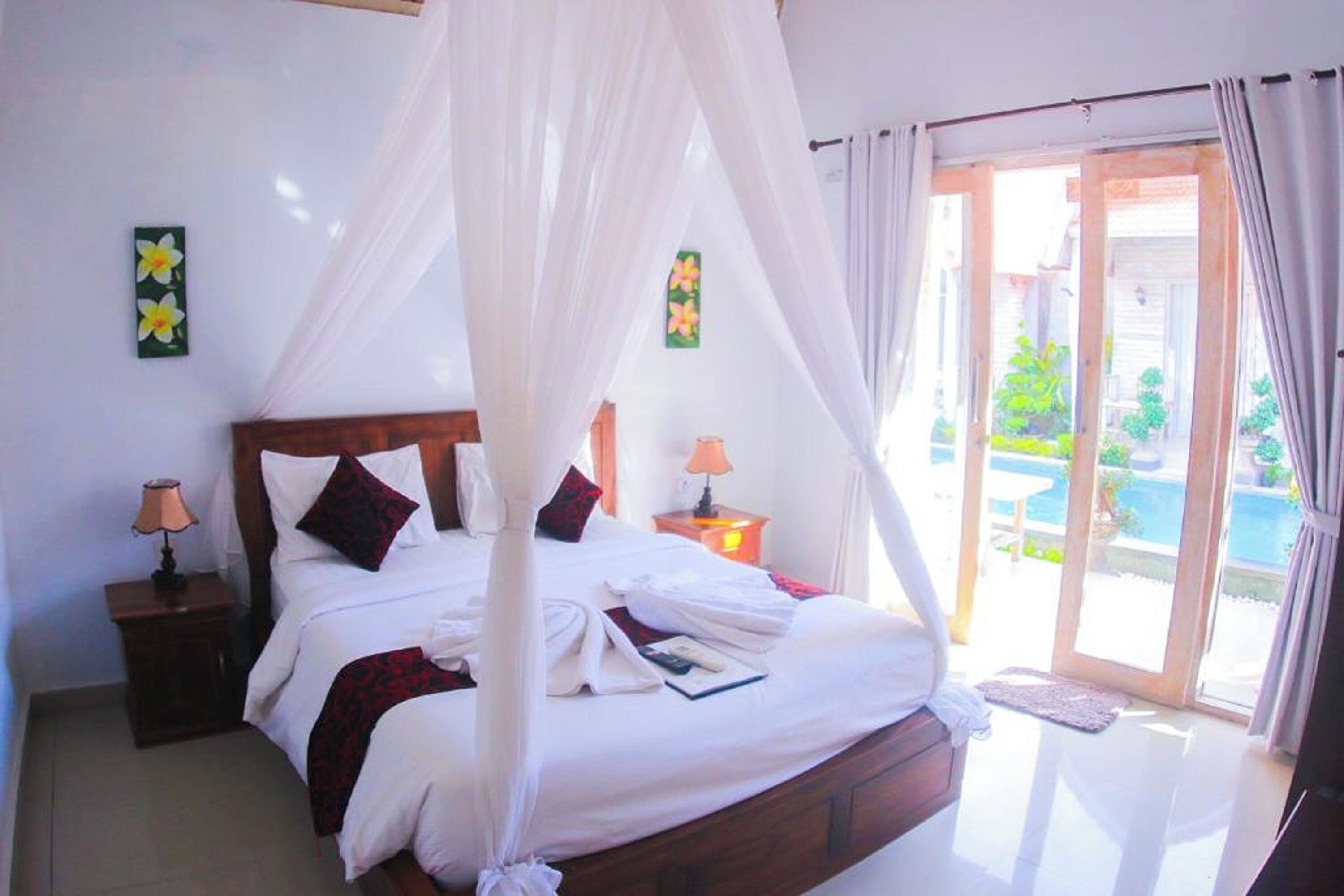 Une chambre à coucher avec un lit à baldaquin, deux lampes de chevet et une vue sur une piscine, visible à travers une porte vitrée.
