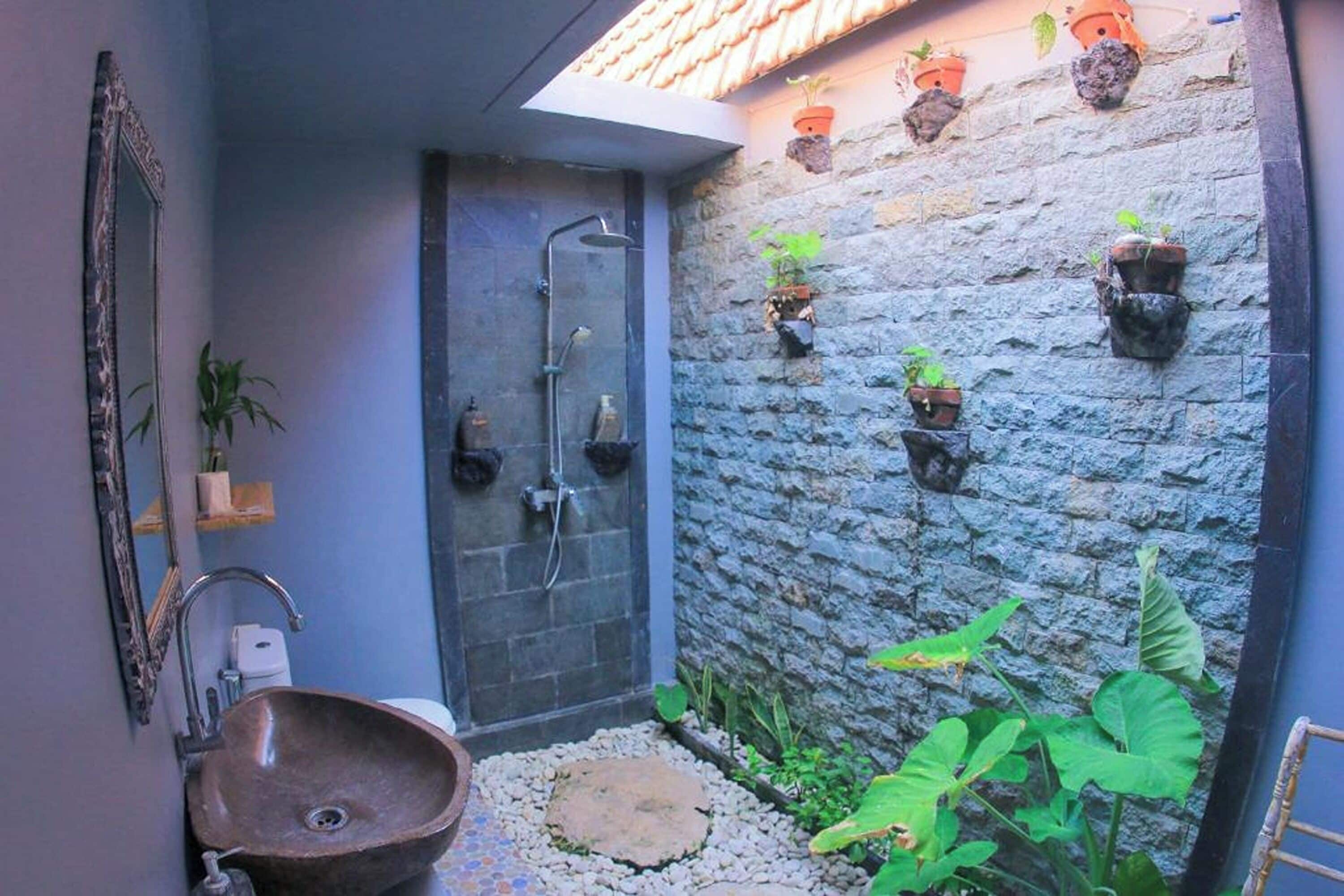 A bathroom with a stone wall, a sink, a shower, and potted plants.