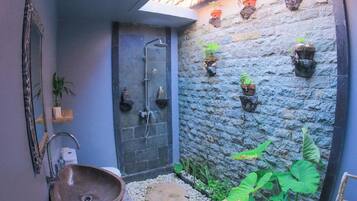 A bathroom with a stone wall, a sink, a shower, and potted plants.