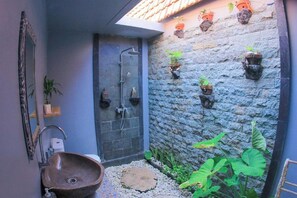 A bathroom with a stone wall, a sink, a shower, and potted plants. - The Box Paradise Bungalow (Penida Island)