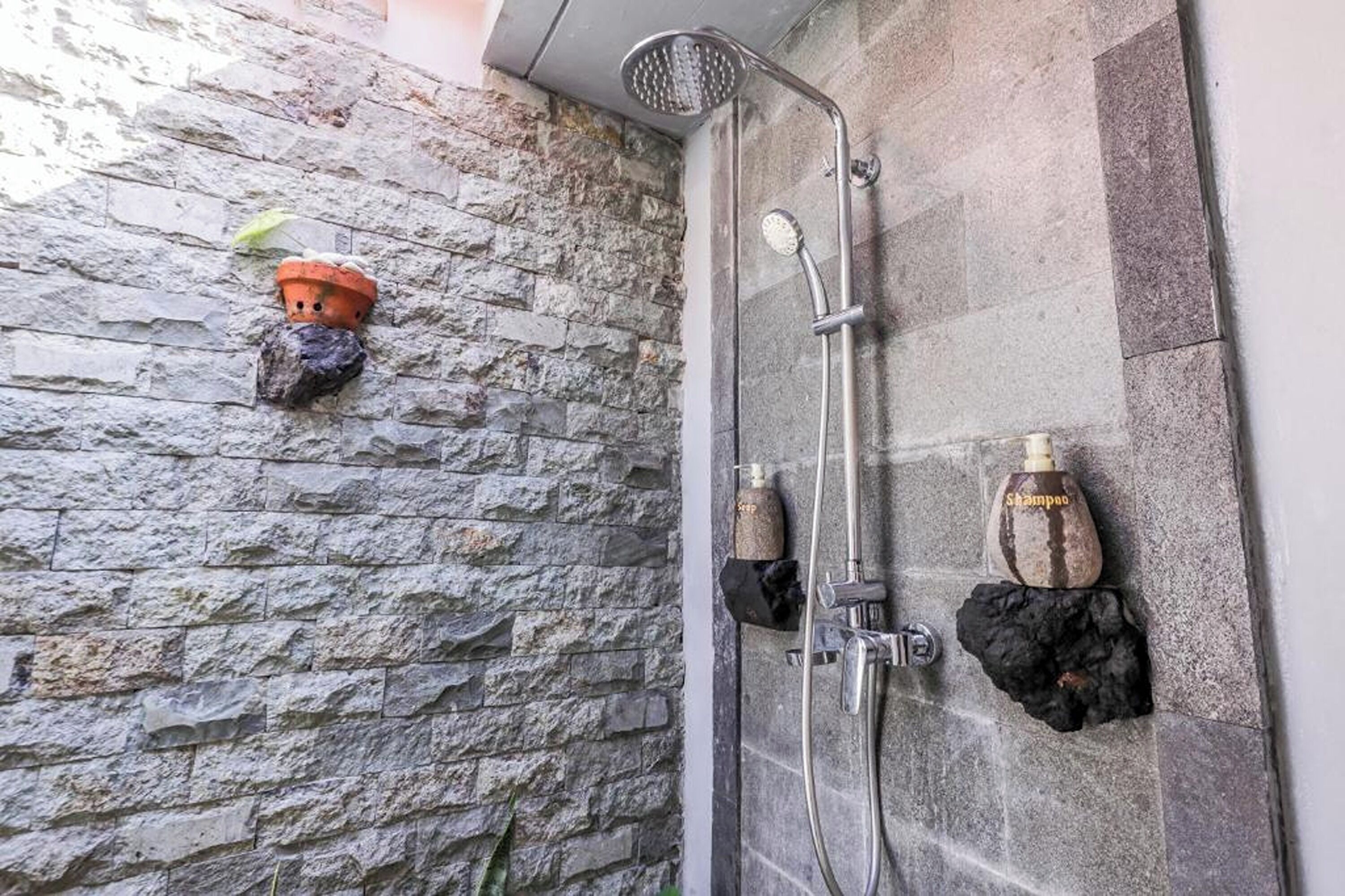 A shower area with a stone wall, a handheld showerhead, and two bottles of shampoo.