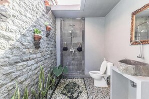 A bathroom with a stone wall, a shower, a toilet, and a sink with a stone basin.