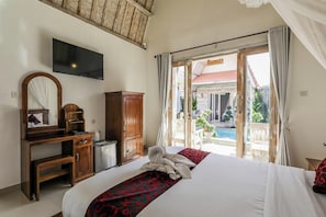 A hotel room with a bed, a desk, a television, and a view of a pool and outdoor area.