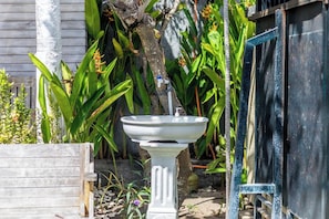 A white outdoor sink with a faucet, surrounded by greenery and a wooden structure. - The Box Paradise Bungalow (Penida Island)