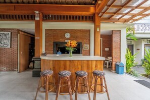 Una zona con barra de madera, pared de ladrillo, un reloj y un jarrón con flores.