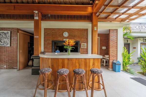 Uma área de bar com balcão de madeira, parede de tijolos, um relógio e um vaso com flores.