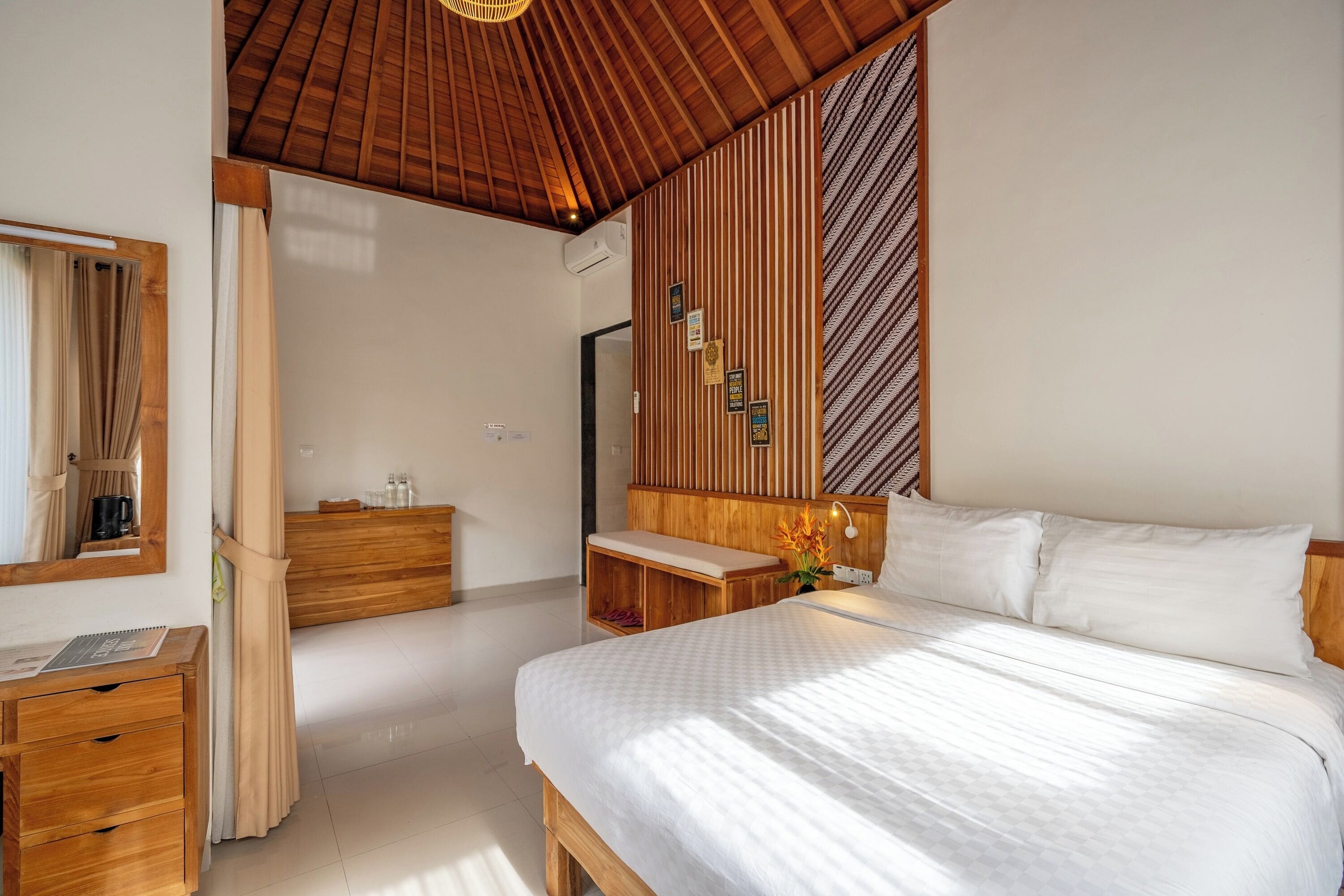Ein Schlafzimmer mit Holzboden, einem Bett mit weißer Bettwäsche, einer hölzernen Kommode, einem Spiegel und einer Wand-Klimaanlage.