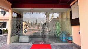 Entrada de um hotel com um tapete vermelho, portas de vidro e vista para a rua.