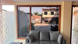 Um sofá cinzento num quarto com uma janela grande, um esfregão no chão e uma parede parcialmente visível com um logotipo.