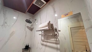Casa de banho com parede de mármore, um porta-toalhas, área de duche e sistema de ventilação.