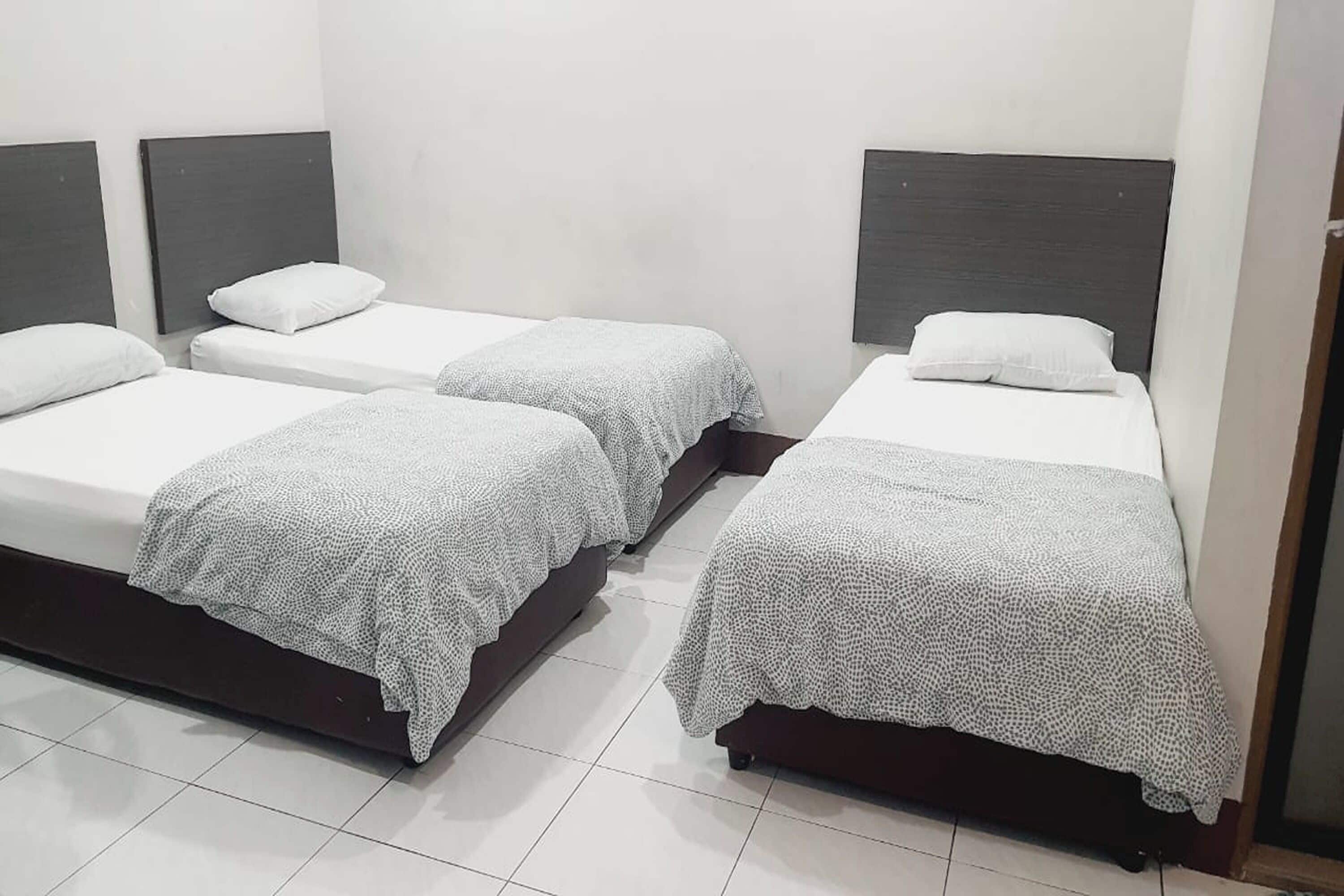 Ett hotellrum med tre separata sängar, var och en med en vit kudde och ett mönstrat täcke.
