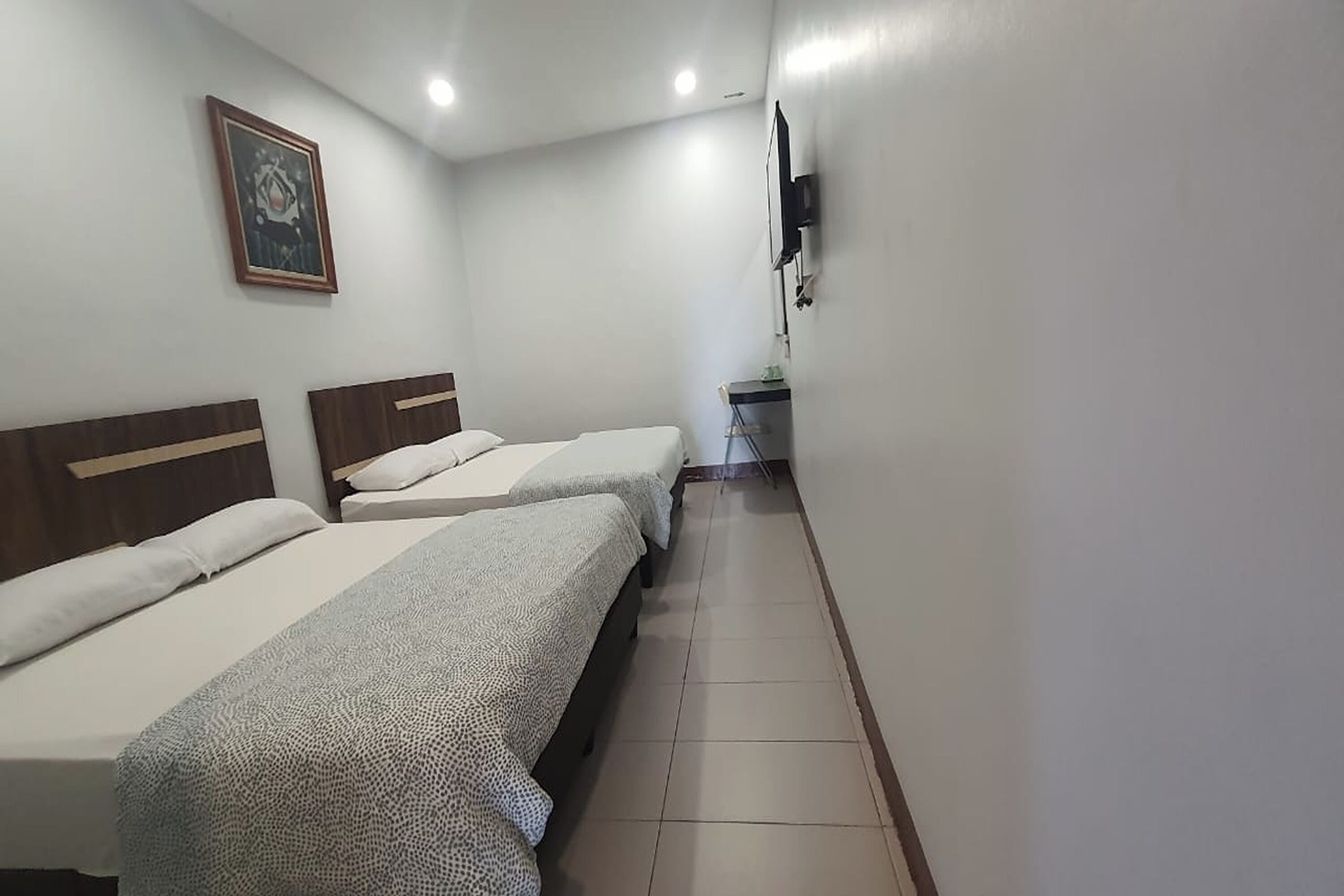 Una camera d'albergo con due letti, una televisione a parete e un piccolo tavolo con una sedia.