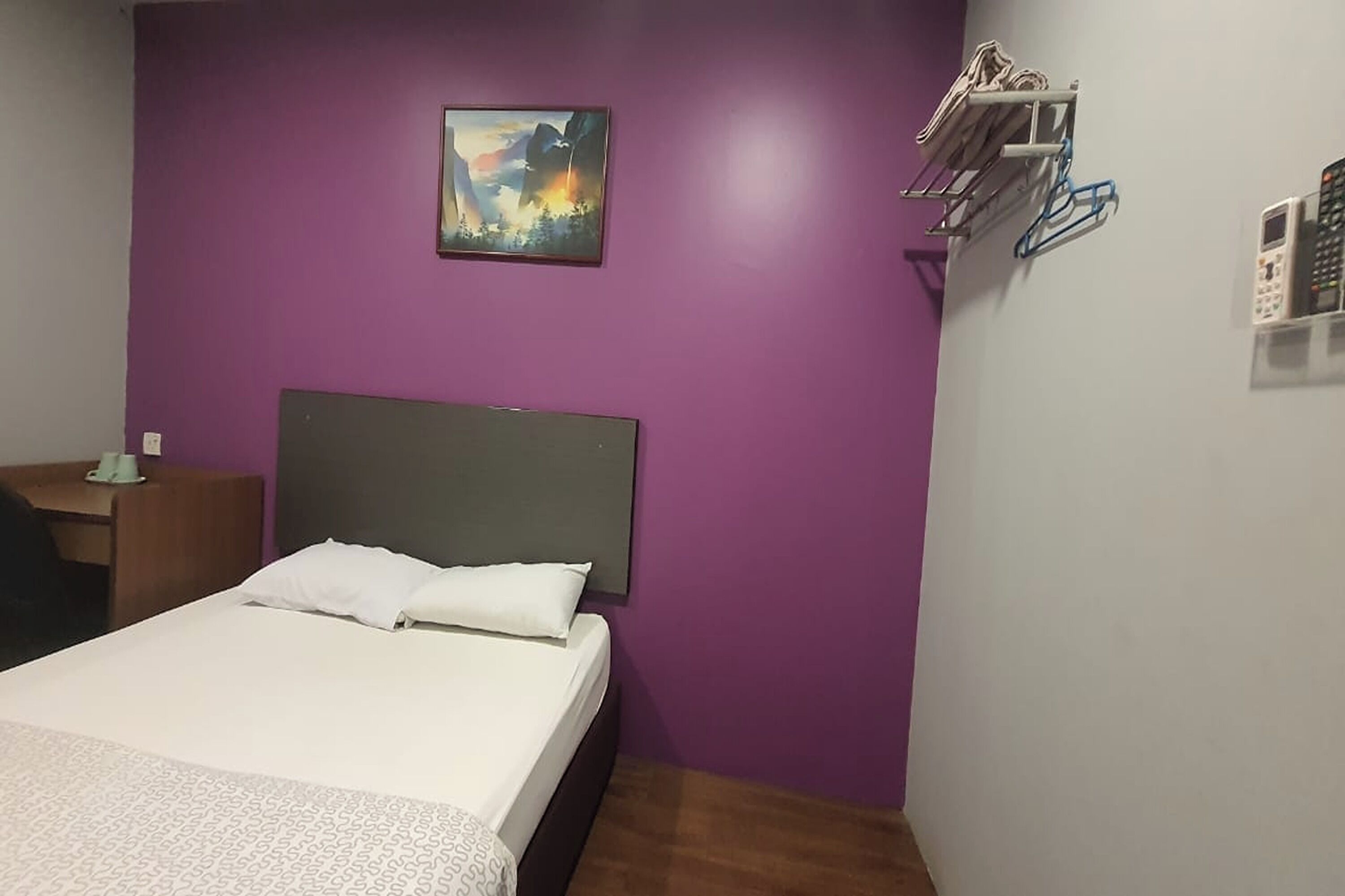 A bedroom with a bed, a nightstand, a painting, and a wall-mounted shelf with items.