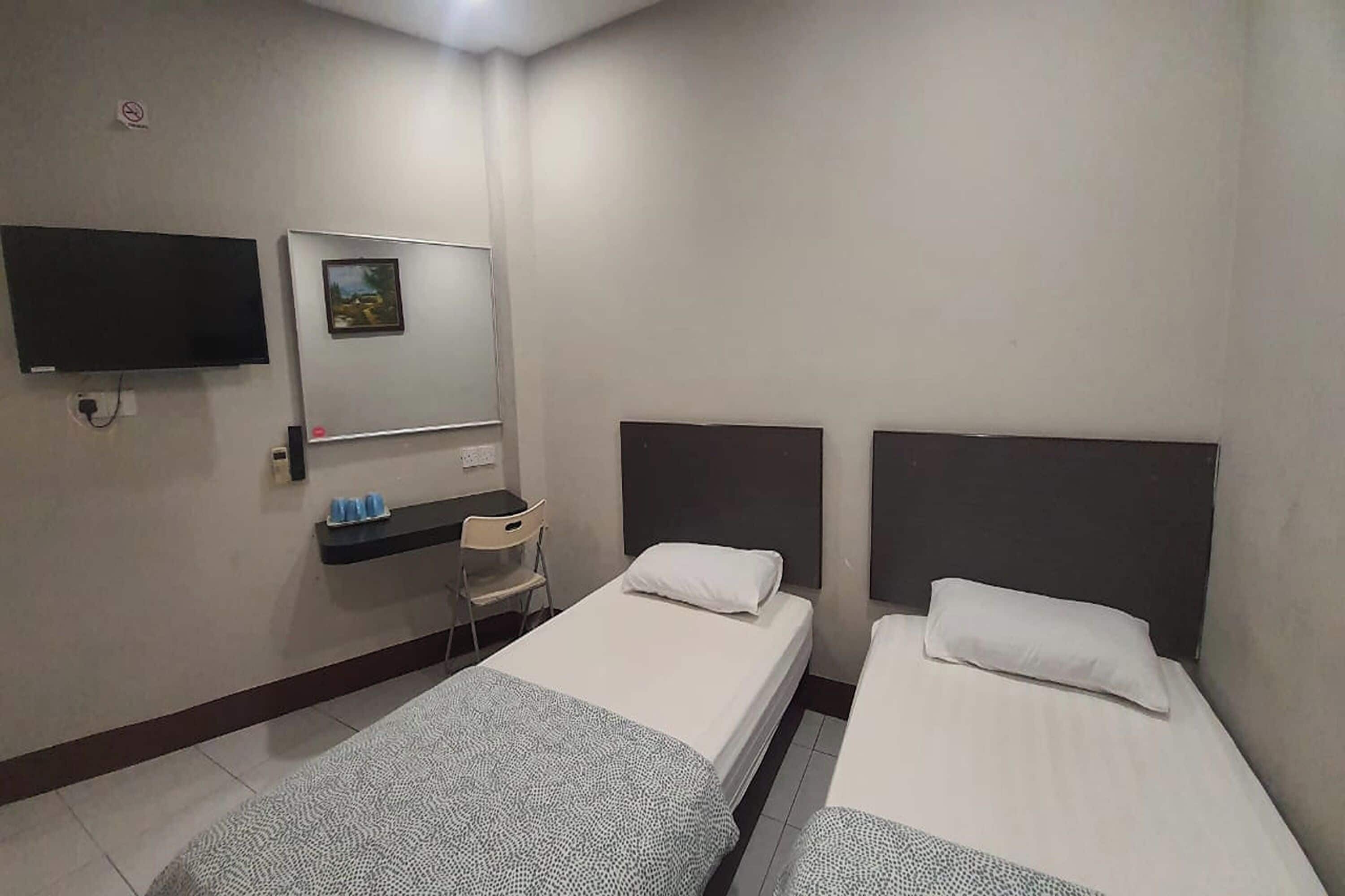A hotel room with two single beds, a small desk, a chair, a television, and a mirror.