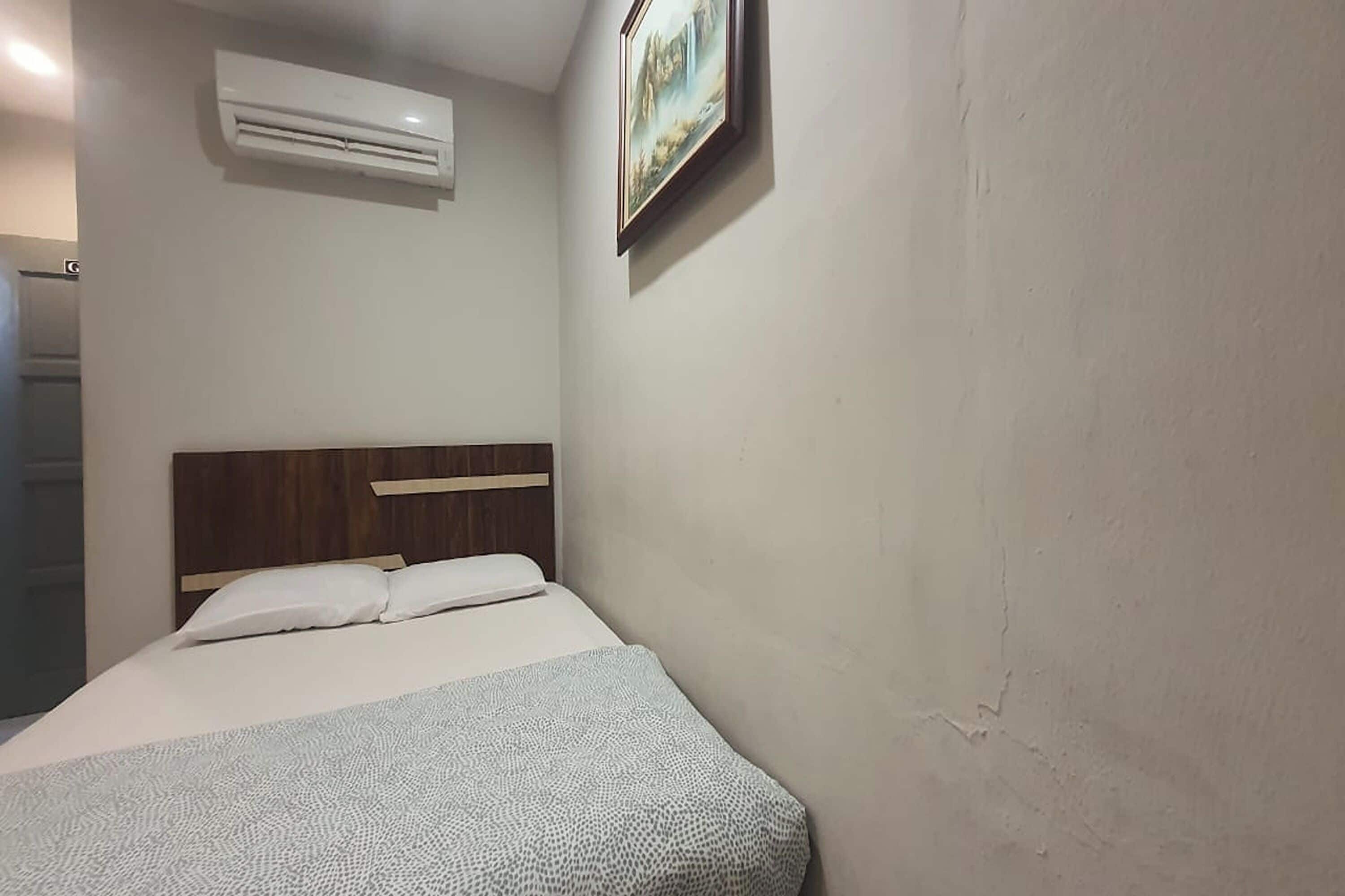 Una habitación con una cama, un equipo de aire acondicionado y un cuadro en la pared.