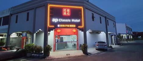 A hotel with a neon sign, a contact number, and a visible entrance.
