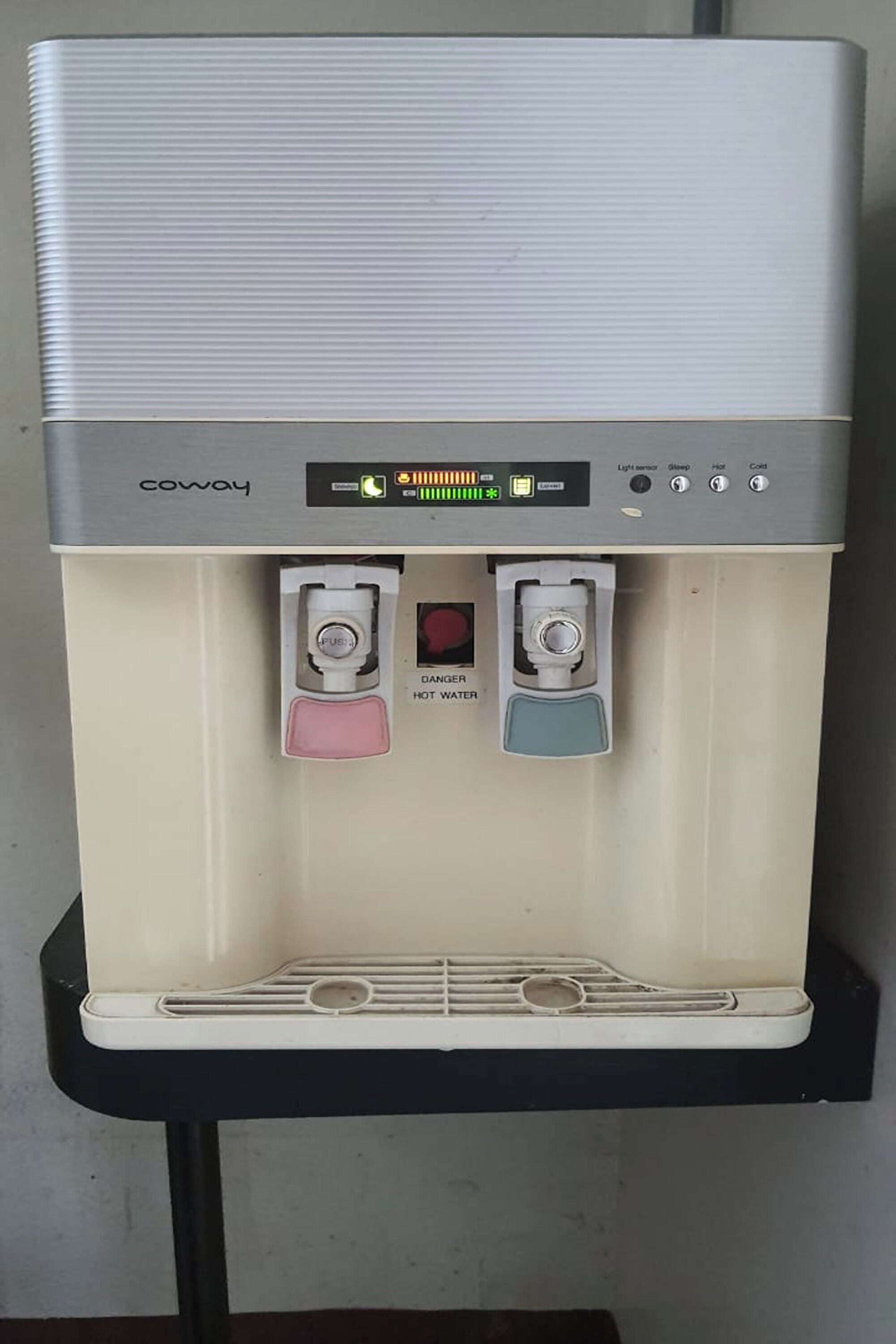Een waterdispenser met een digitaal scherm, twee tappen voor warm en koud water, en een knop om water te tappen.