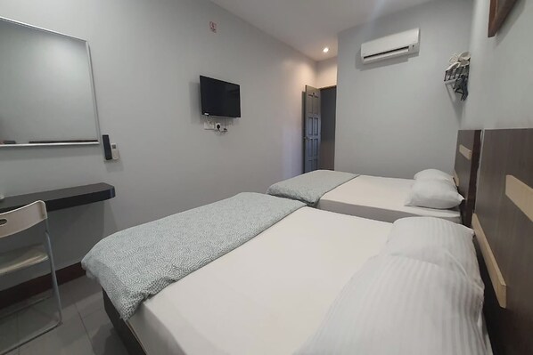 A hotel room with two beds, a flat-screen TV mounted on the wall, a bedside table, and an air conditioning unit.