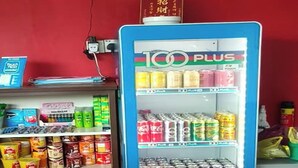 En automat med et udvalg af drikkevarer og snacks, et sikkerhedskamera monteret på væggen, og et skilt med kinesiske tegn.