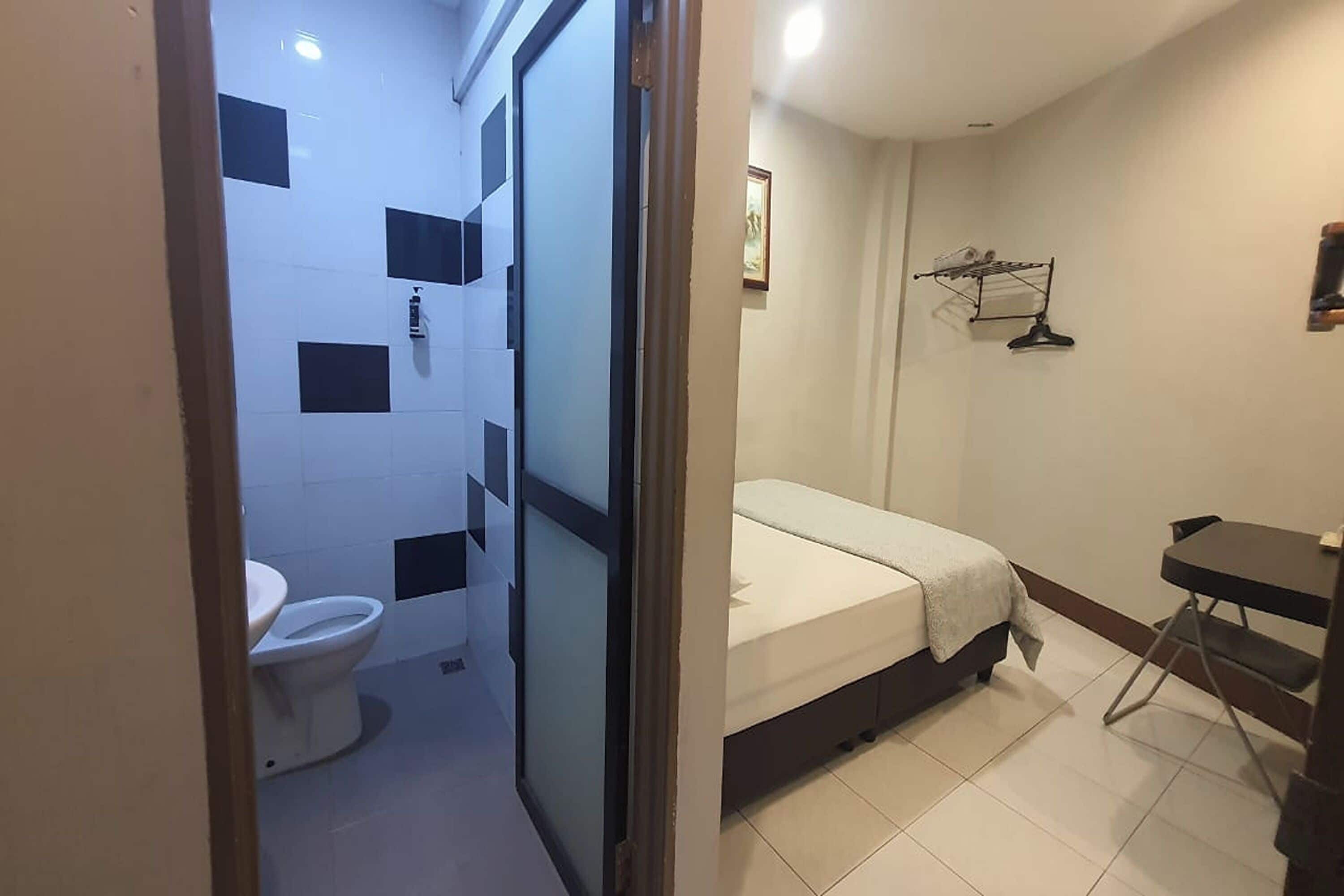 Una habitación pequeña y funcional con inodoro, cama y una mesita.