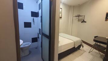 Una habitación pequeña y funcional con inodoro, cama y una mesita.