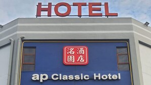 Et hotel med et tydeligt 'HOTEL' skilt øverst, en facade i rødt og blå, og et kontaktnummer nedenunder.