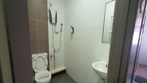 Et lille badeværelse med fliser, toilet, vask og brusebad.