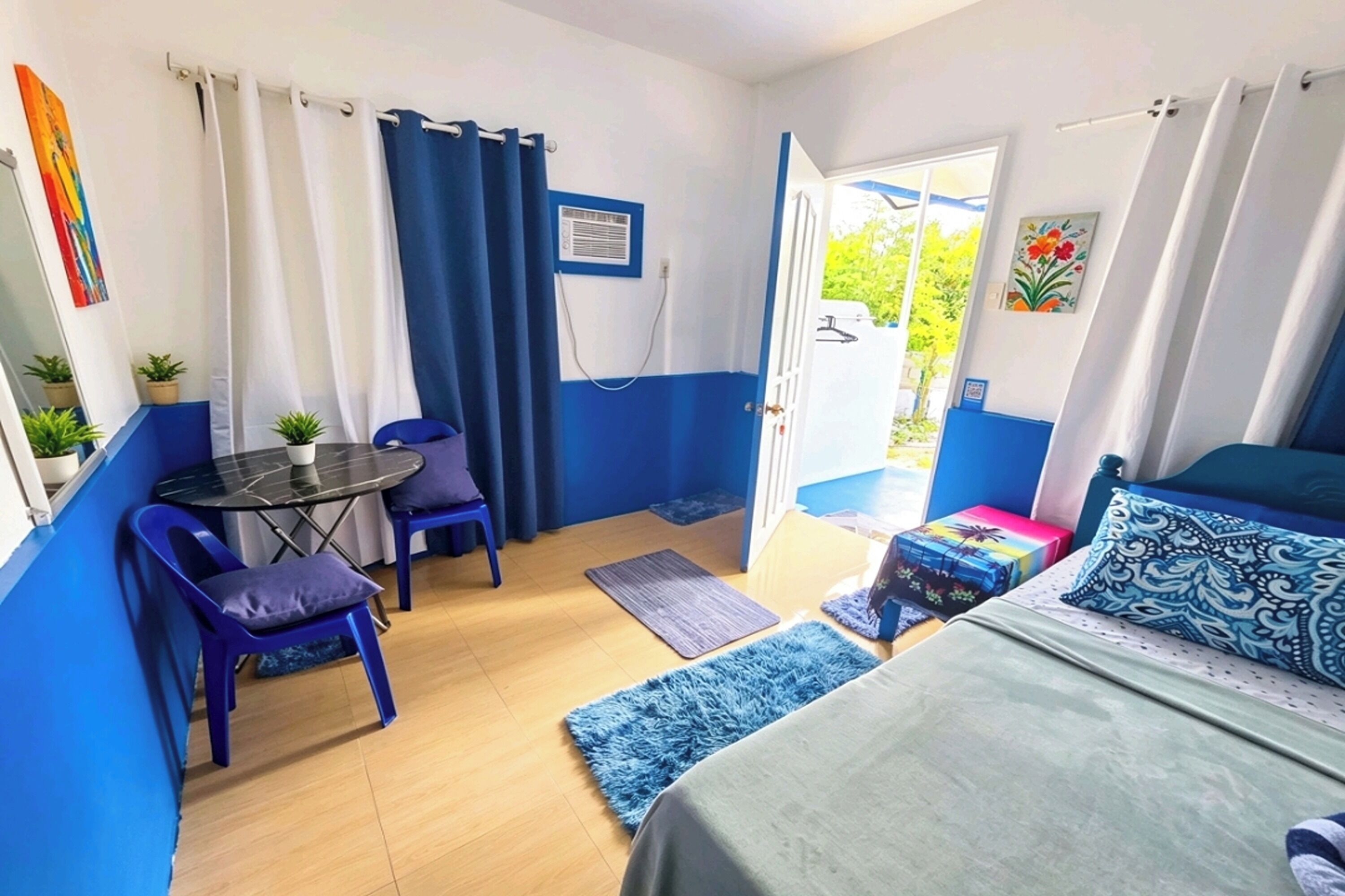 Una stanza con un letto, un tavolo, due sedie, un piccolo tappeto e una porta che dà sull'esterno.
