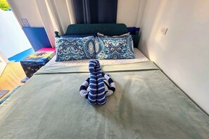 A bed with patterned pillows and a striped stuffed toy in a room with a window and curtains.