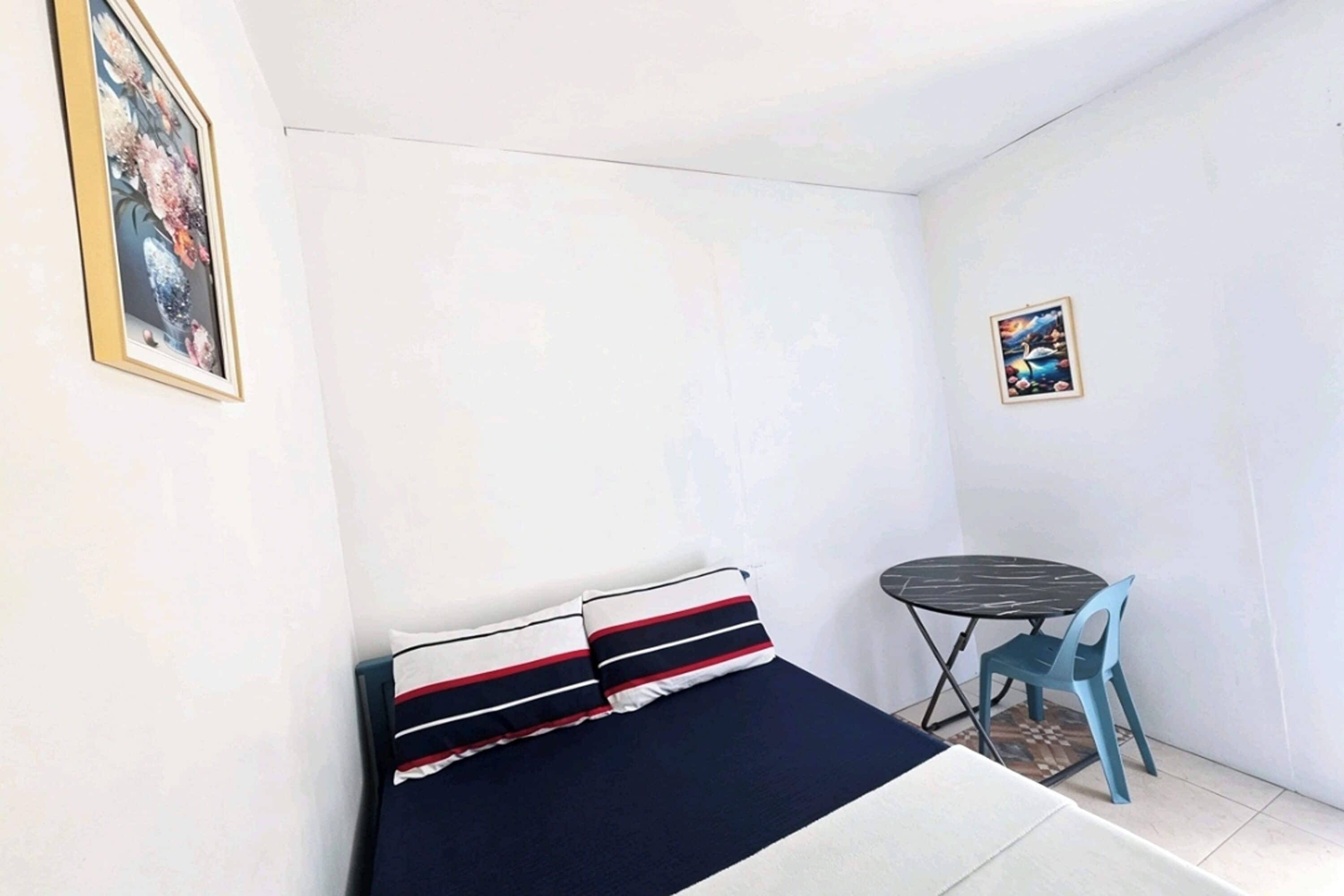 Una habitación pequeña y funcional con cama, mesa y dos sillas.