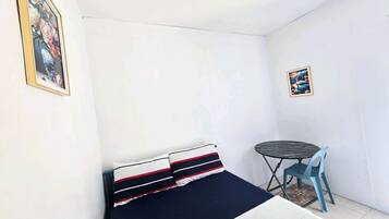 Una habitación pequeña y funcional con cama, mesa y dos sillas.