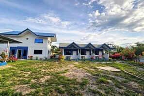 A residential building with a blue roof and white walls, featuring a front garden with potted plants and flowers. - B'Lu Bamboo (Moalboal)
