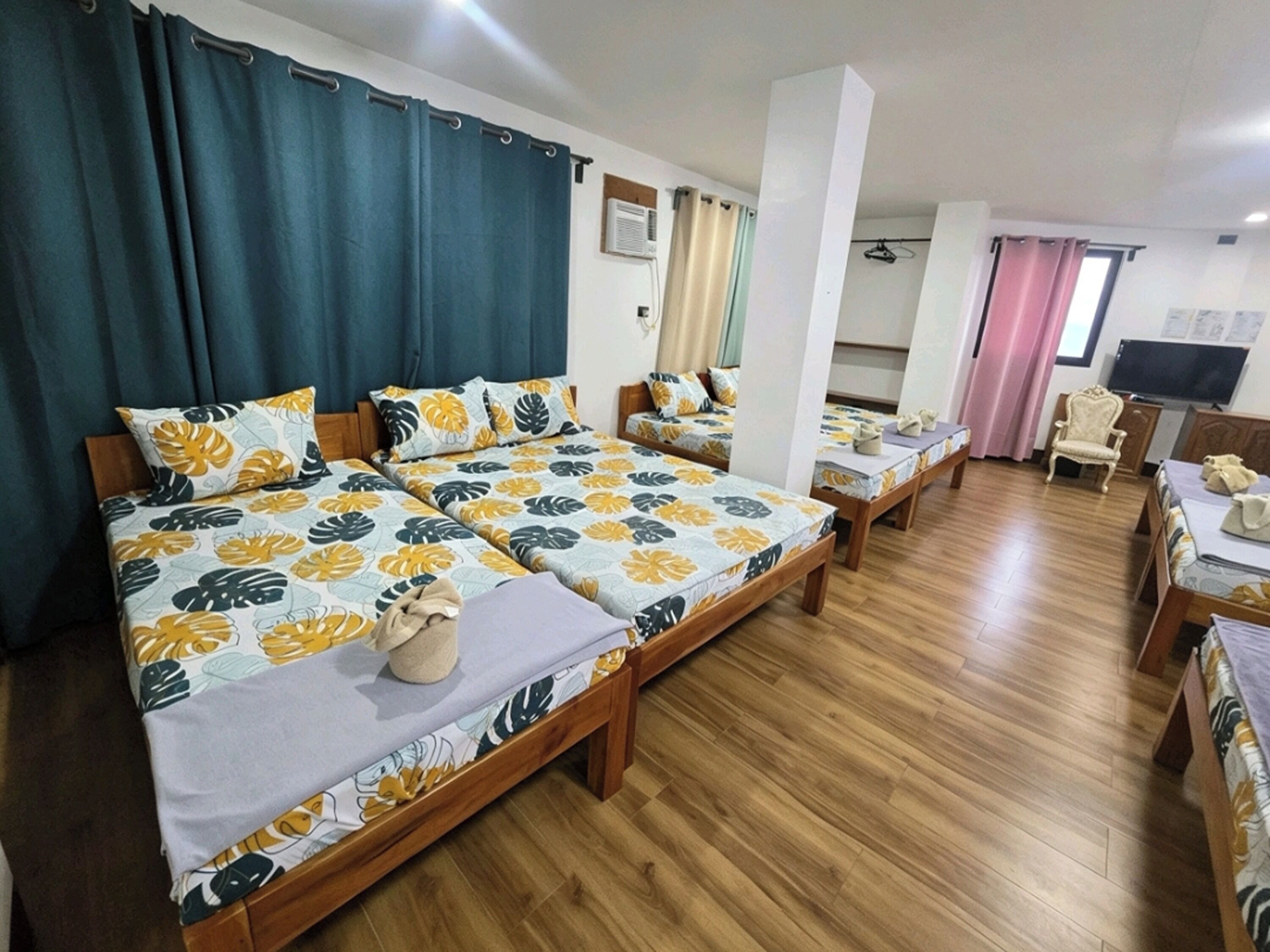 Een hotelkamer met twee bedden, houten vloeren, een televisie en een stoel.