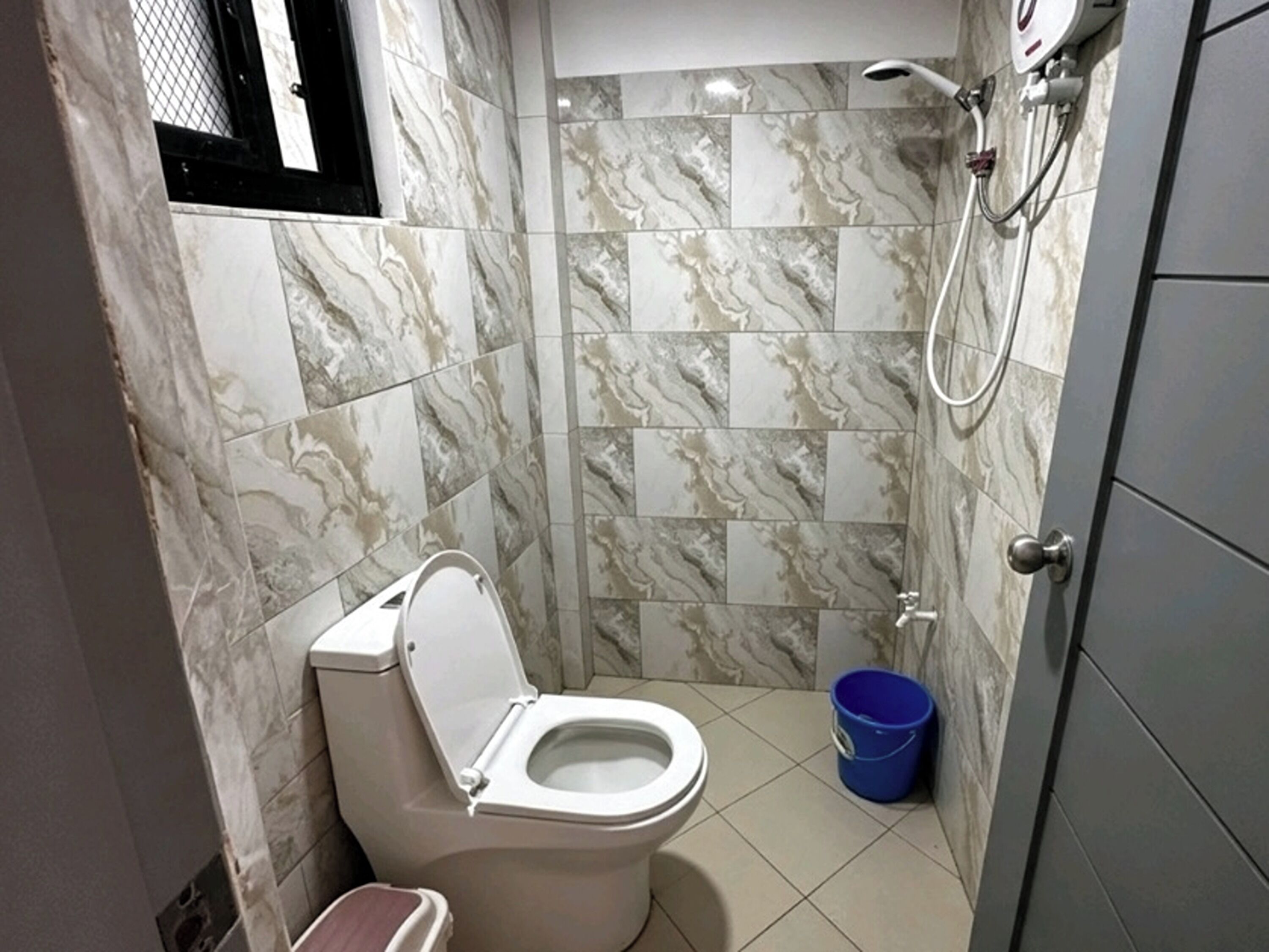 A bathroom with a toilet, shower, and a blue bucket.