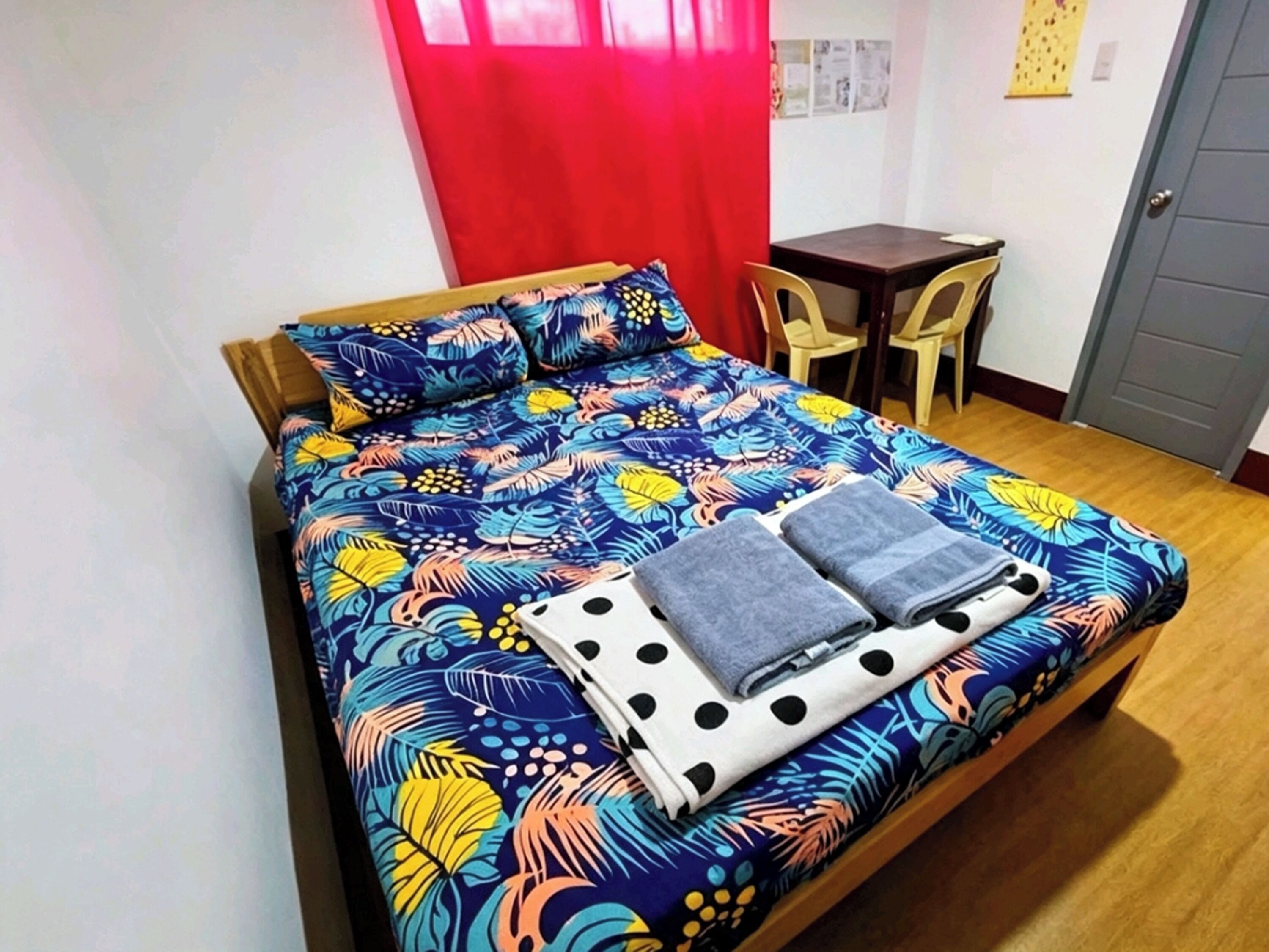 A bed with a floral bedspread, two pillows, and two folded towels. There is a small table and two chairs in the room.