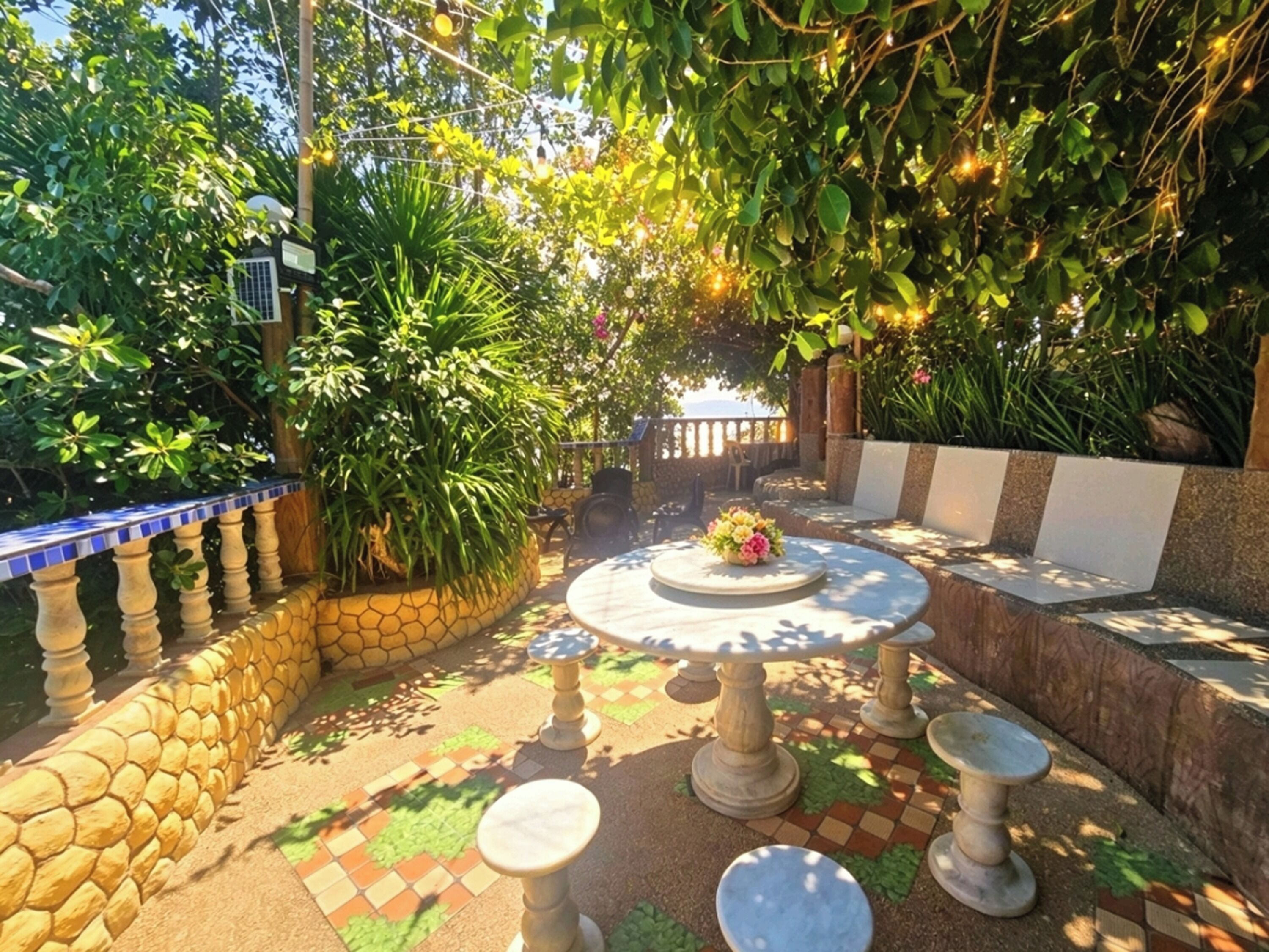 A patio with a round table and stools, surrounded by a stone wall and potted plants.